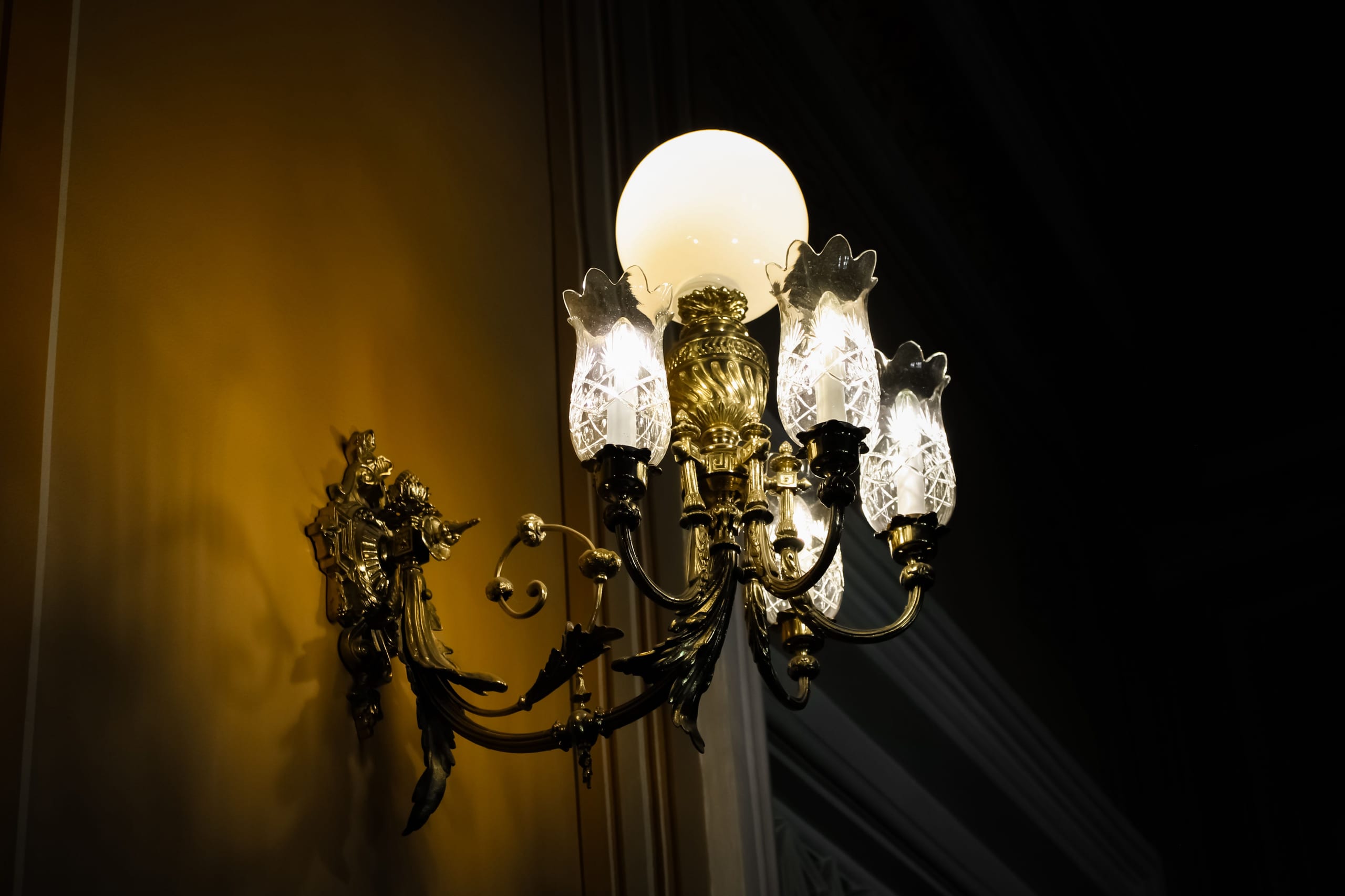 A wrought-iron candle-style wall lantern glowing in a dim entry hall